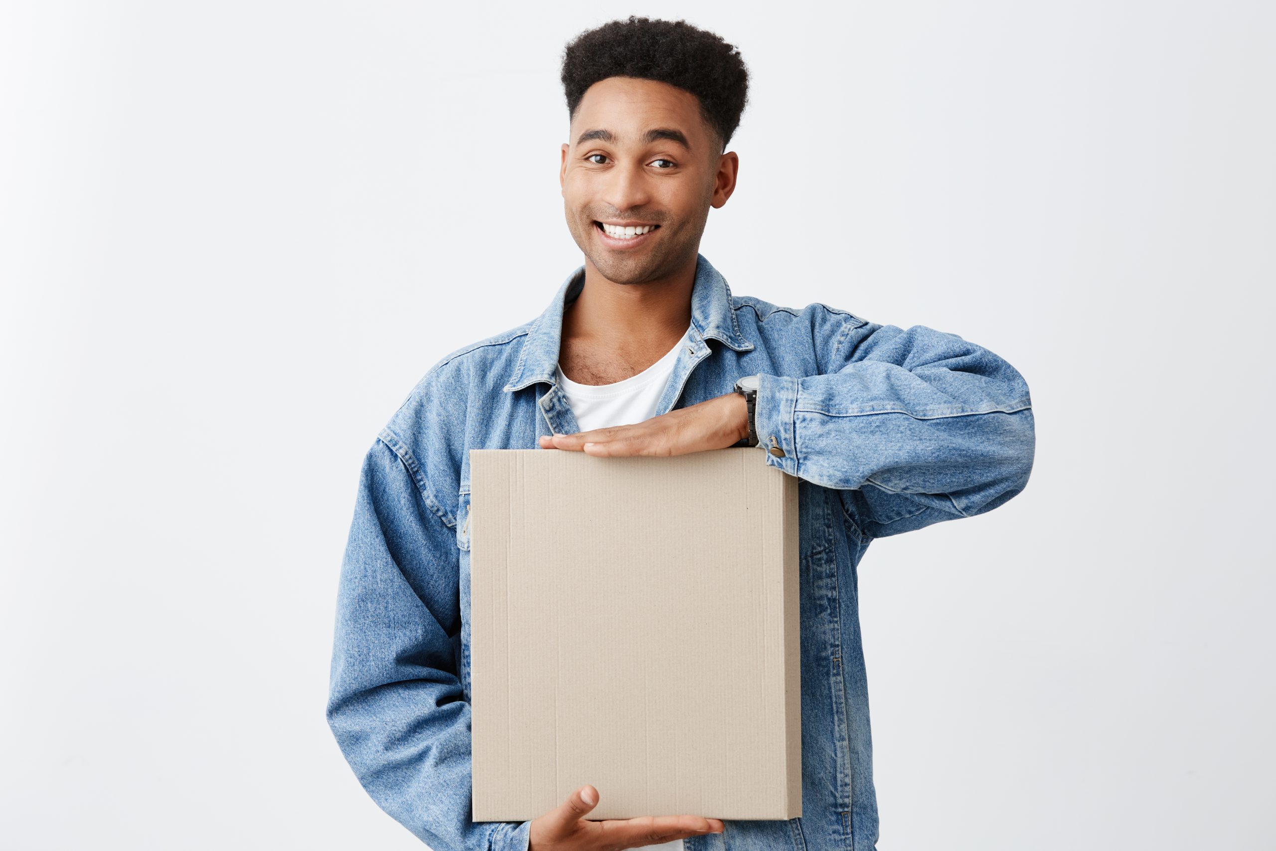 Portrait of young cheerful attractive dark-skinned man with afro hairstyle in white shirt and blue jacket holding paper box in hands with bright smile and happy expression.